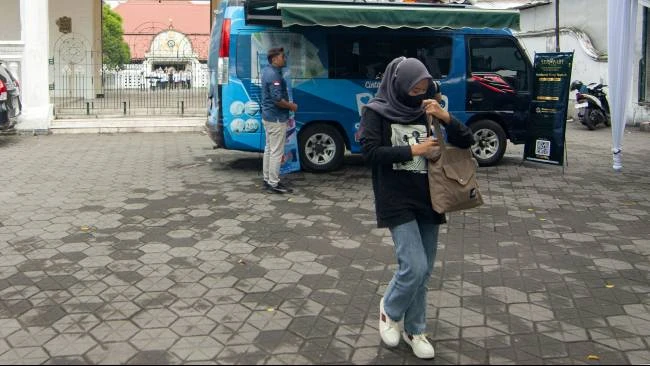 Seorang perempuan berjalan meninggalkan lokasi mobil penukaran uang keliling milik Bank Indonesia, seusai menukar sejumlah uang di halaman Masjid Besar Kauman, Yogyakarta, Selasa (11/3/2025). 