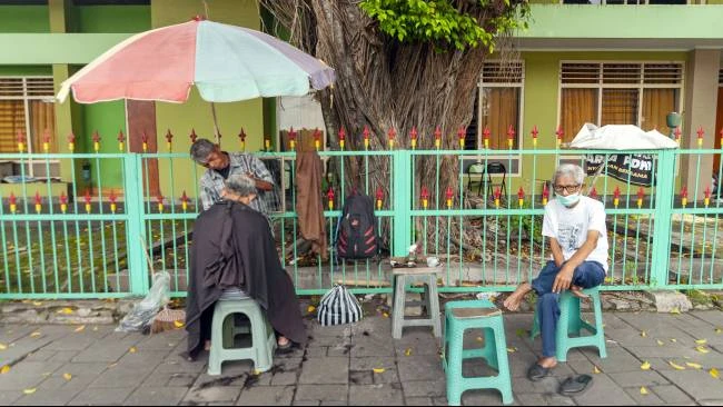 Seorang pelanggan menunggu giliran untuk dicukur oleh Udin, di kawasan Alun-Alun Utara, Kota Yogyakarta, Minggu (30/3/2025).