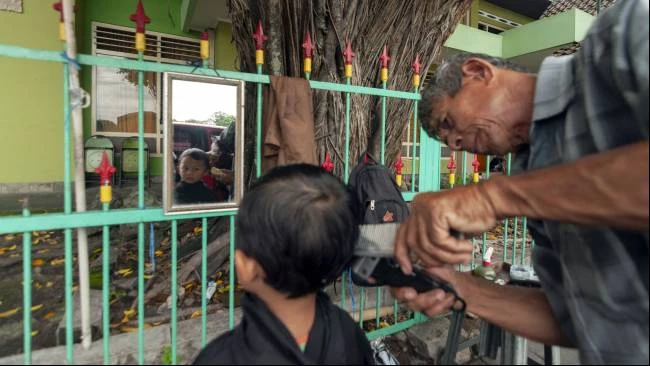 Seorang bocah terlihat tenang saat Udin mencukur rambutnya di kawasan Alun-Alun Utara, Kota Yogyakarta, Minggu (30/3/2025).