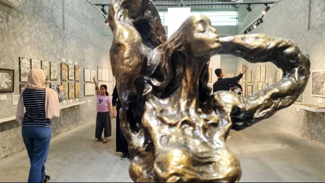 Seorang wanita memotret bocah perempuan dengan latar gambar sketsa dan ilustrasi karya Win Dwi Laksono, yang dipamerkan di Equalitera Art Space, Bantul, Daerah Istimewa Yogyakarta, Minggu (13/7/2025). 