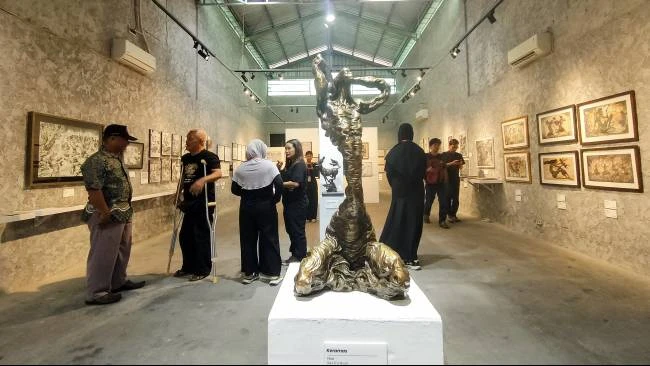 Seniman Win Dwi Laksono (menggunakan tongkat) berbincang dengan pengunjung pameran sketsa dan ilustrasi karyanya di Equalitera Art Space, Bantul, Daerah Istimewa Yogyakarta, Minggu (13/7/2025).
